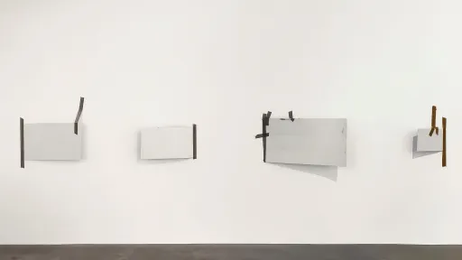 vier Skulpturen hängen an der Wand. Weisse Platten mit dunklem Klebeband