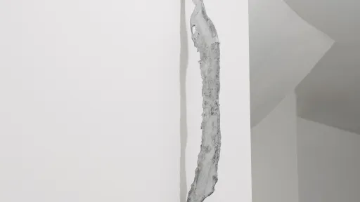 An einer weissen Wand hängt eine weiss-gräuliche Skulptur.