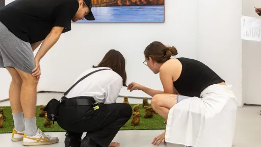 Drei junge Menschen bücken sich über eine Miniaturwelt auf dem Boden eines Ausstellungsraumes