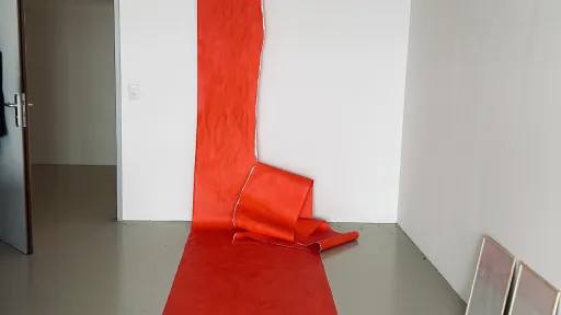 ein langes, rotes Stück Papier mit einem langen Riss darin hängt von der Decke, der Wand und dem Boden entlang