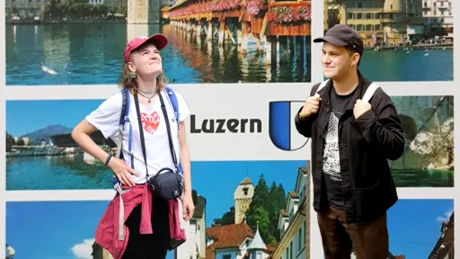 Die Kunstvermittler:innen stehen vor einer alten Postkarte Luzerns. Sie sind gekleidet in Touristen-Kleidung
