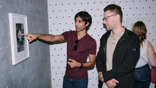 Zwei Männer zeigen auf einen schwarzweissen Druck an der Wand