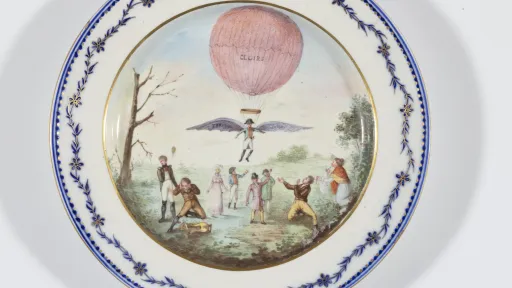 Ein antiker Teller mit Malerei einer Person die an einem Ballon hängt. Die Person trägt Flügel.